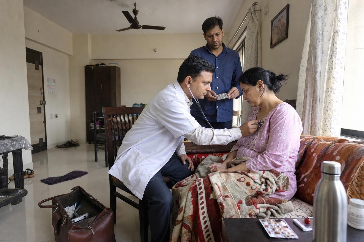 A Healkin doctor examining a patient in her own living room, his bag open on the floor beside him
