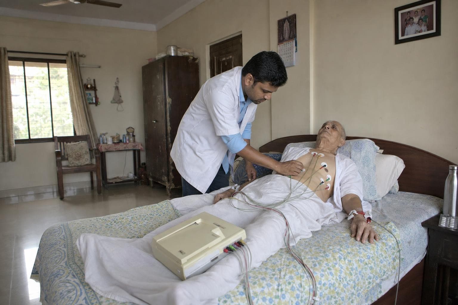 A Healkin technician placing ECG electrodes on an elderly patient lying in his own bed at home