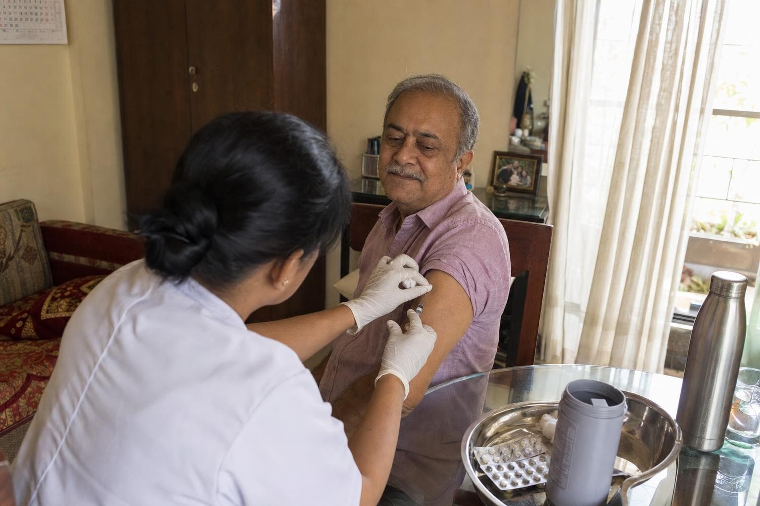 A Healkin nurse administering a vaccine to a seated patient at home